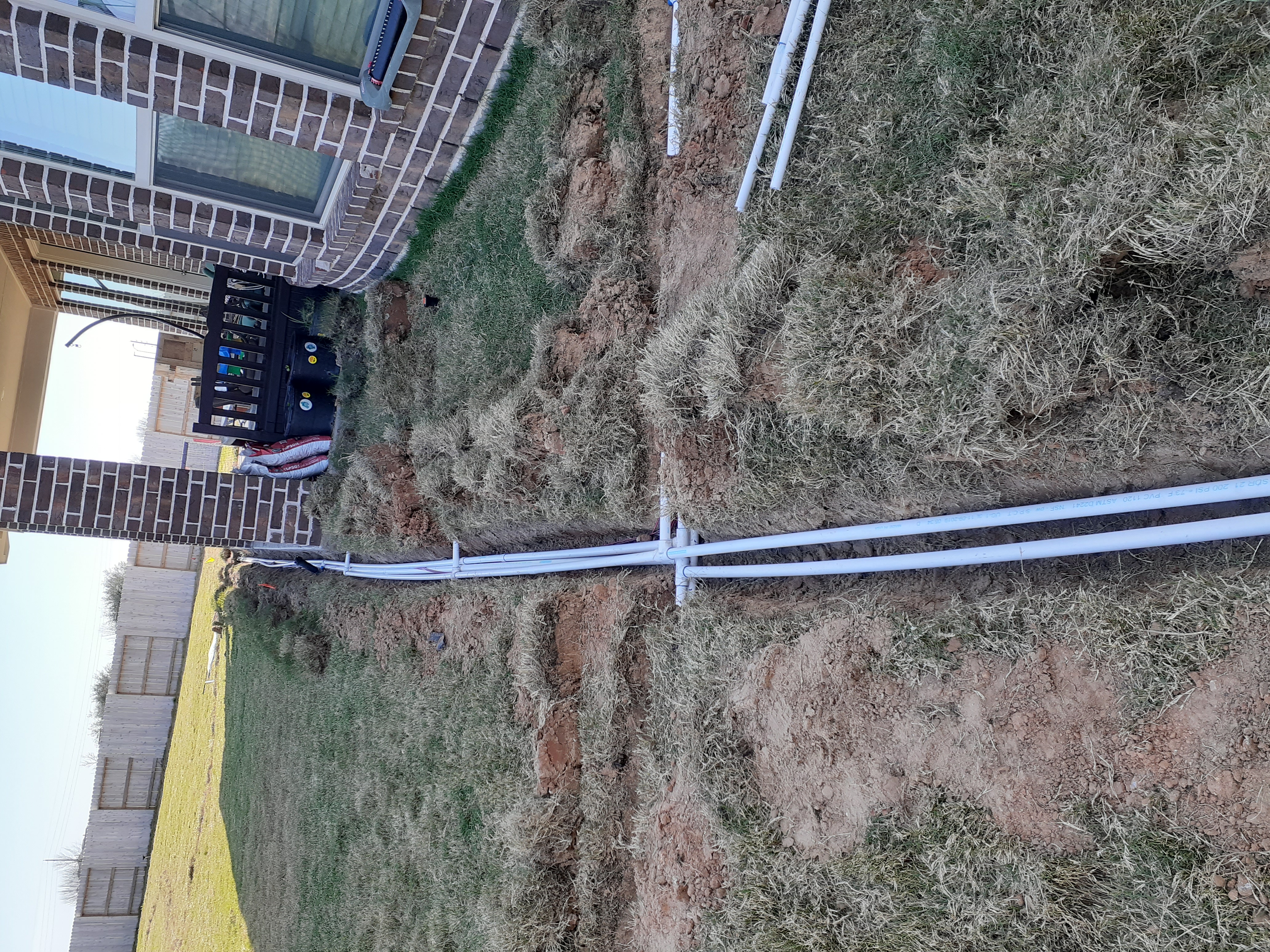 Multiple PVC supply lines branching from the manifold and routing across the yard at the Glencorse property