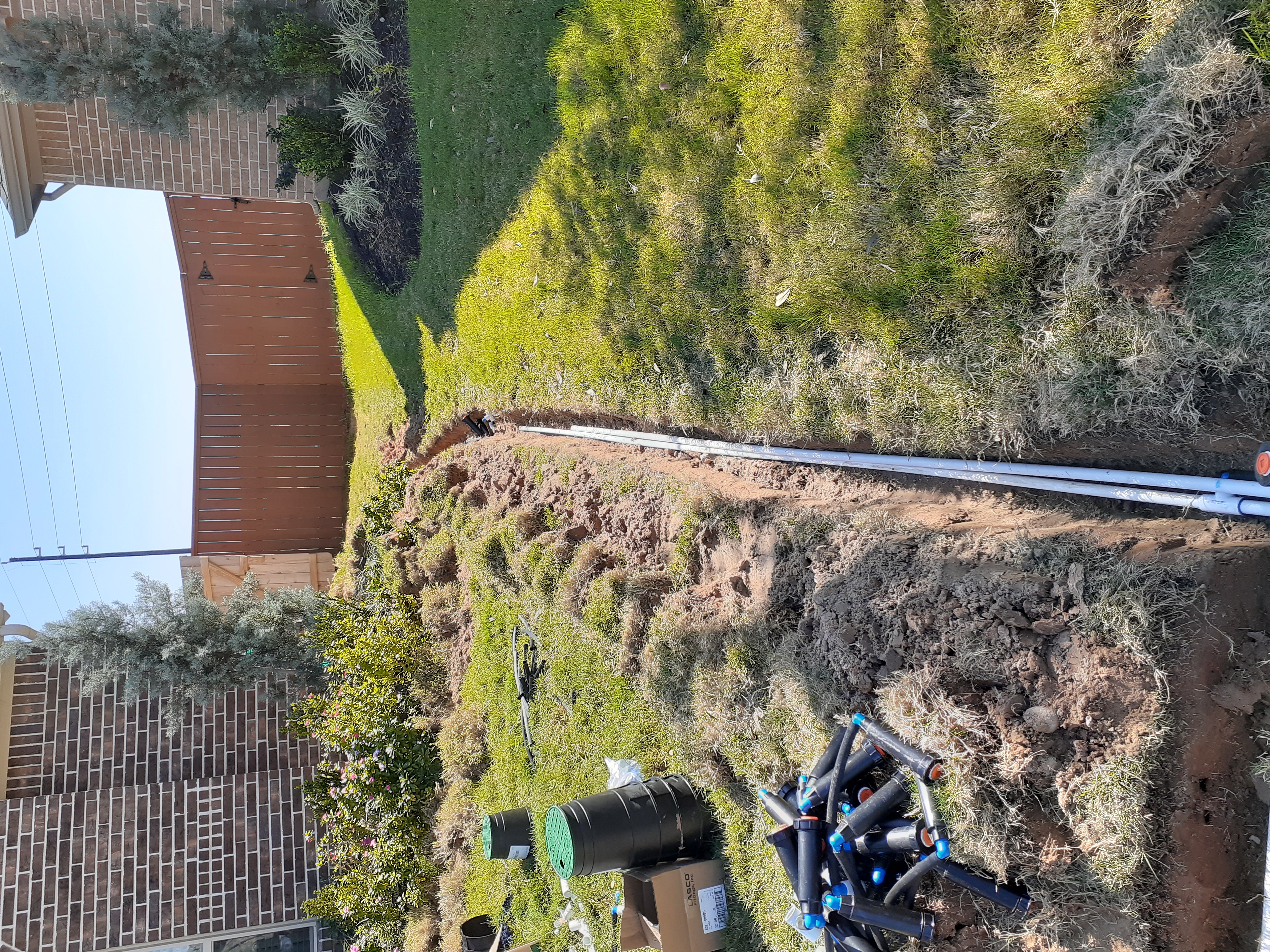 Full-yard view of the Glencorse irrigation install in progress — fresh trench cut across the lawn
