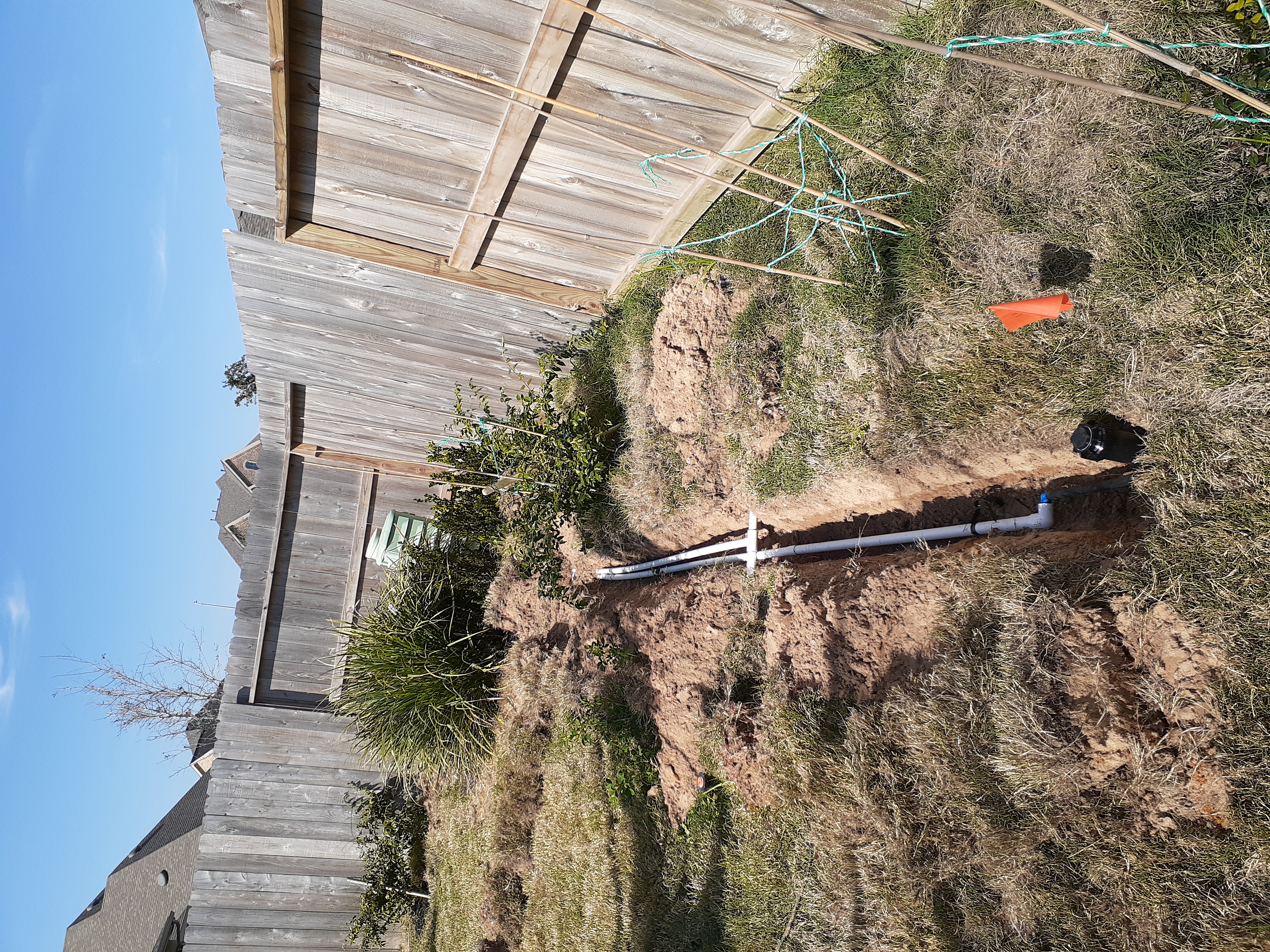 Side-yard view of the trench routing PVC past the deck at the Glencorse property