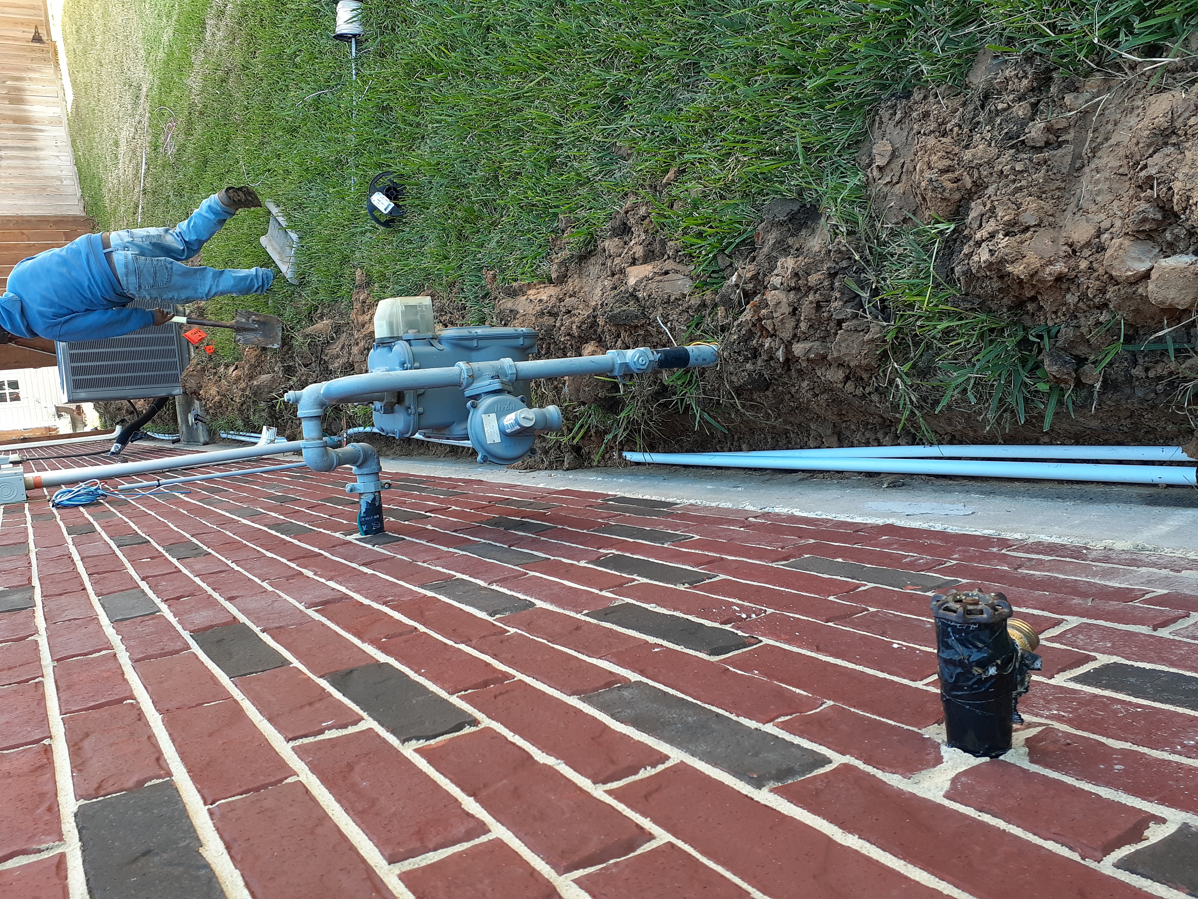 Backflow preventer assembly mounted on a brick wall with a technician working in the trench behind it